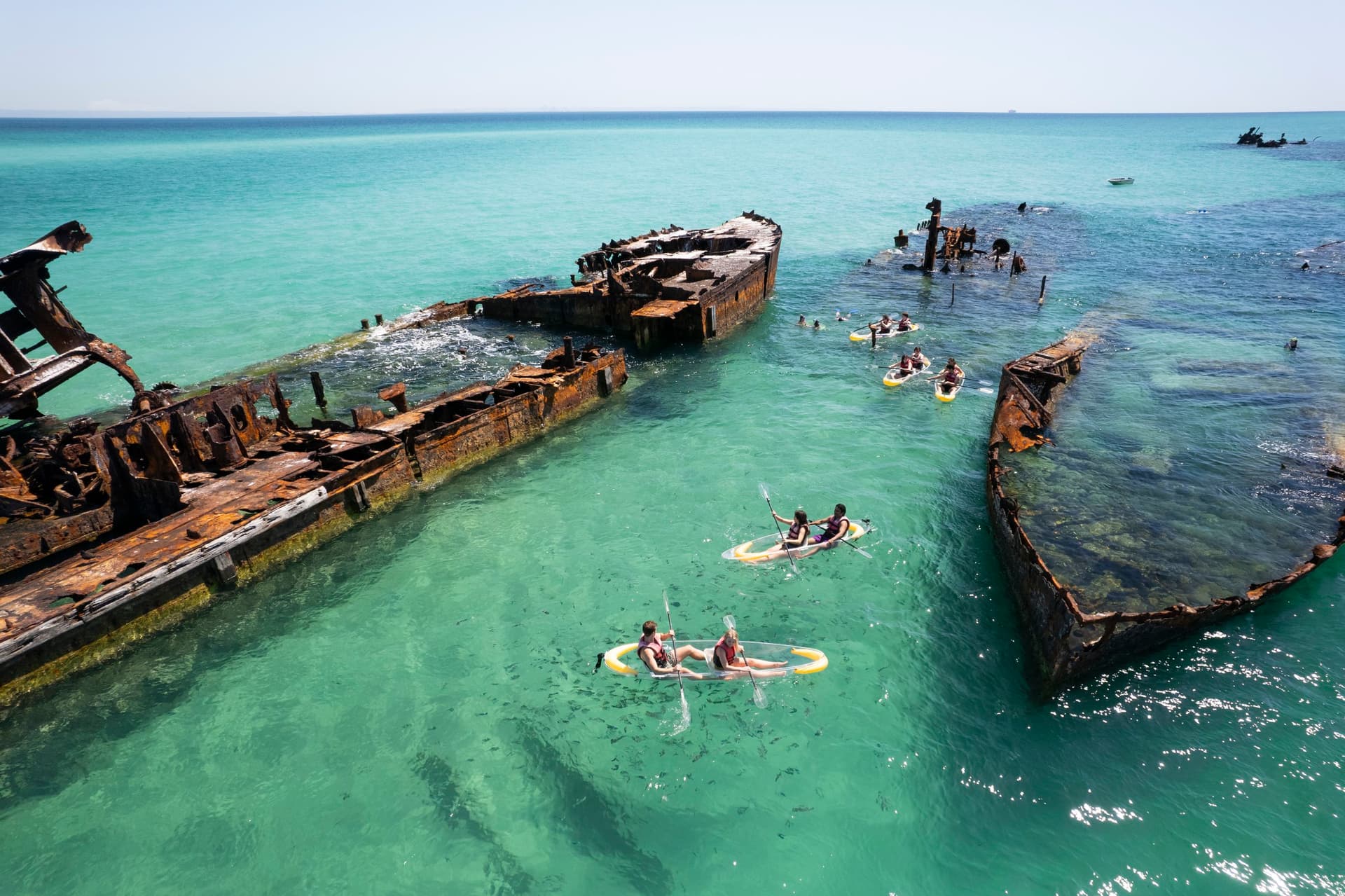 People kayaking around a shipwreck in crystal clear water